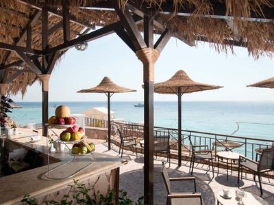 Überdachte Terrasse mit Tischen und Stühlen direkt am Meer mit Strohhut-Sonnenschirmen.