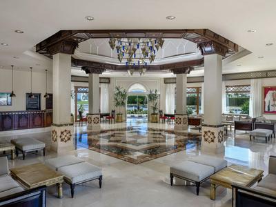 Großer Hotel-Lobby-Bereich mit Stühlen, Marmorboden und kunstvollem Kronleuchter.