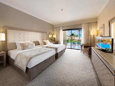 Modern eingerichtetes Hotelzimmer mit zwei Betten und Blick auf einen Pool.