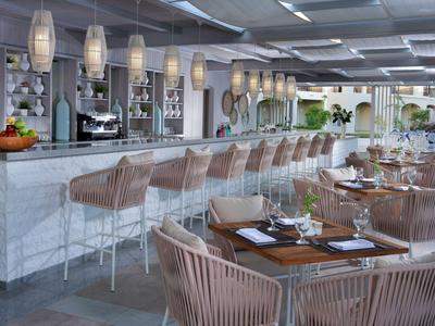 Moderner Hotelbarbereich mit weißen Lampen, gepolsterten Hockern und metallischen Sitzgruppen.
