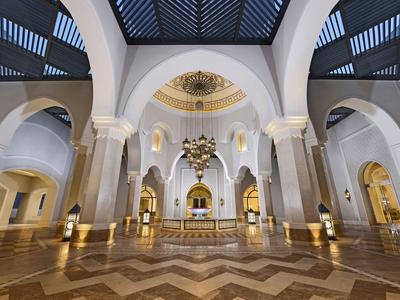 Großer Hotel-Lobby mit hohen Bögen, einer zentralen Brunneninstallation und opulenten Verzierungen.