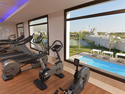 Fitnessraum mit modernen Geräten und großer Fensterfront mit Blick auf Pool und Garten.