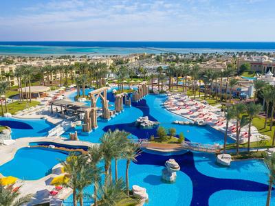 Großer Hotelpoolbereich mit blauen Wasserflächen, Palmen und Blick aufs Meer im Hintergrund.