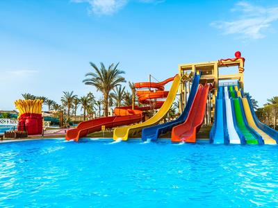 Großer Hotelpool mit Lagunen, Palmen und Liegestühlen in Küstennähe bei sonnigem Wetter.