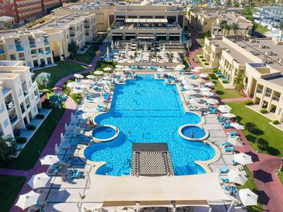 Großes Hotel mit zentralem, blauem Pool und vielen Sonnenschirmen nachts beleuchtet.