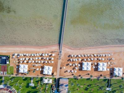 Luftaufnahme eines Strandes mit Strandliegen, Sonnenschirmen und einem langen Steg ins Meer.