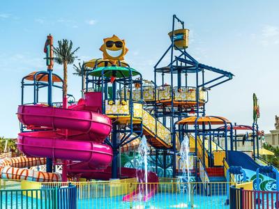 Buntes Wasserspielplatz mit pinker Rutsche und Palmen im Freien unter blauem Himmel.