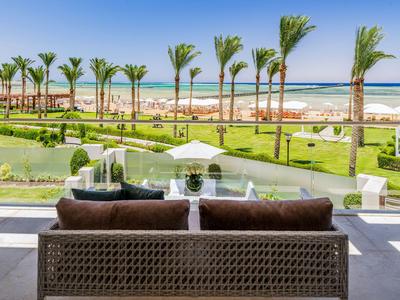Blick von einer Terrasse mit Sofa auf einen Garten mit Palmen und Meer im Hintergrund.