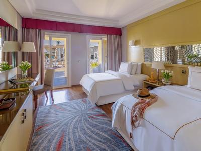 Helles Hotelzimmer mit zwei Betten, Schreibtisch, Stuhl und Zugang zum Balkon.