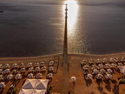 Strand mit Sonnenschirmen und einem hohen Turm vor ruhigem Wasser bei Sonnenuntergang.