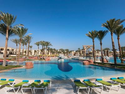 Großer Pool mit Sonnenliegen und Palmen bei klarem Himmel in einem Hotelresort.