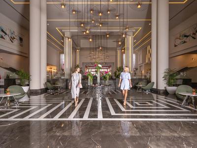 Zwei Frauen laufen durch eine elegante Hotelhalle mit Marmorboden und modernen Möbeln.