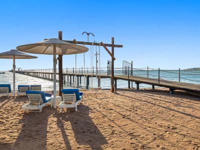 Strand mit Sand, Liegestühlen, Sonnenschirmen und einem Steg, der ins Wasser führt.