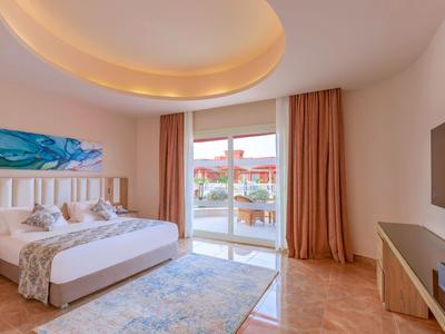 Elegantes Hotelzimmer mit Doppelbett, großem Fenster, Vorhängen und modernem TV an der Wand.