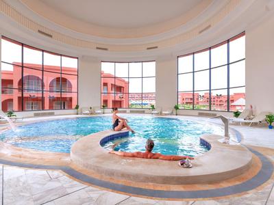Innenbereich mit rundem Whirlpool und großen Fenstern mit Blick auf rote Gebäude und Garten.