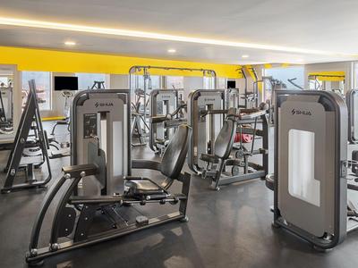 Ein moderner Fitnessraum mit verschiedenen Krafttrainingsgeräten und gelben Akzenten an den Wänden.
