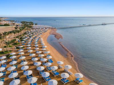 Langer Sandstrand mit weißen Sonnenschirmen und Palmen, angrenzend an ruhiges, blaues Meer.
