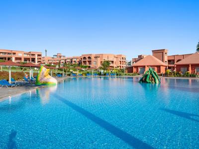 Großer Außenpool mit bunten Wasserspielen vor einem Hotel unter klarem blauem Himmel.