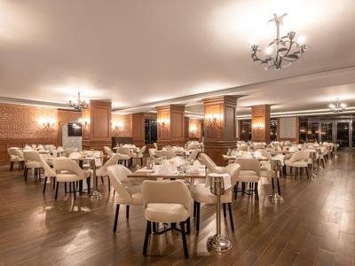 Elegantes Hotelrestaurant mit Holzfußboden, weißen Stühlen und warmem Licht.