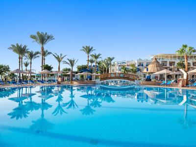 Großer Hotelpool mit klar blauem Wasser, Palmen und Sonnenliegen unter blauem Himmel.