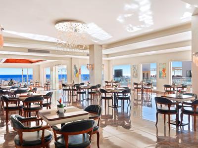 Helles Hotelrestaurant mit modernen Möbeln und Blick aufs Meer durch große Fenster.