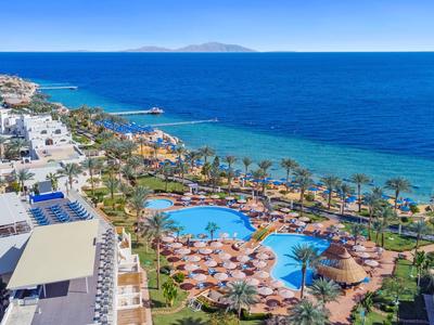 Blick auf ein Strandresort mit Pools, Palmen und direktem Zugang zum blauen Meer.