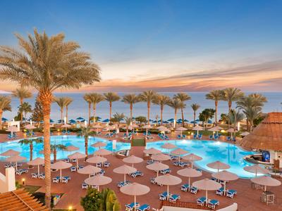Großer Hotelpool mit Palmen, Sonnenschirmen und Liegestühlen bei Sonnenuntergang.