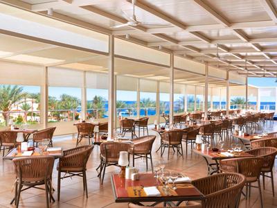 Helle Hotelterrasse mit Holzstühlen und Tischen mit Meerblick bei Tageslicht.