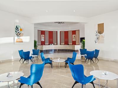 Moderne Hotellobby mit blauen Sesseln, weißen Tischen und hellem Marmorfußboden.
