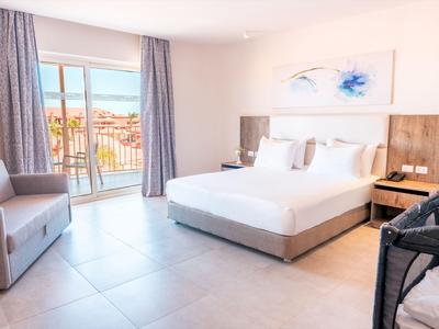 Helles Hotelzimmer mit Doppelbett, Balkon und moderner Einrichtung bei Tageslicht.
