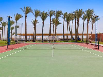 Tennisplatz im Freien mit Palmen und klar blauem Himmel im Hintergrund eines Hotels.