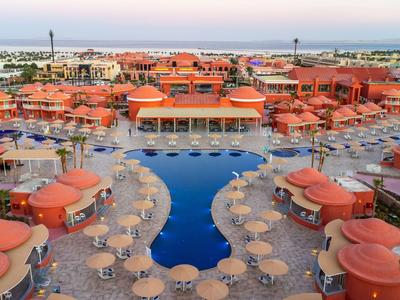 Großes Hotelresort mit Pool, roten Dächern und zahlreichen Sonnenschirmen am Strand.