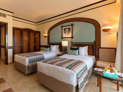 Camera d'hotel con due letti singoli, mobili in legno e decorazioni murali sopra i letti.