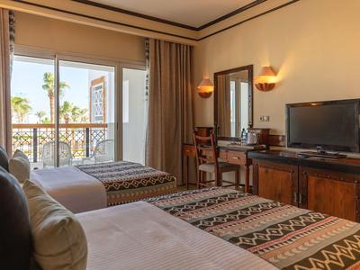 Camera d'hotel con due letti, TV a schermo piatto e balcone con vista sulle palme.