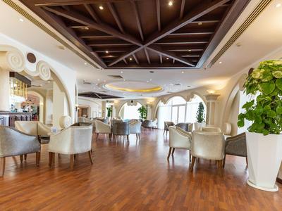 Luminoso atrio dell'hotel con pavimento in legno, sedie comode e grandi piante in vasi bianchi.