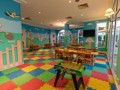 Sala giochi colorata per bambini con tappeti vivaci, tavoli in legno e decorazioni animali alle pareti.