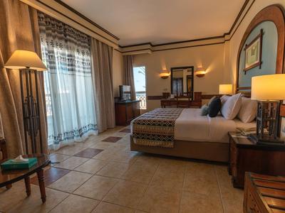 Camera d'hotel luminosa con grandi finestre, letto matrimoniale, pavimento piastrellato e mobili in legno.