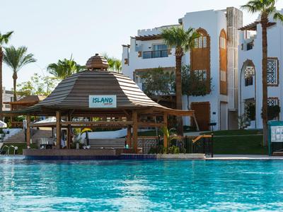 Piscina dell'hotel con bar coperto in ambiente tropicale e edifici moderni sullo sfondo.