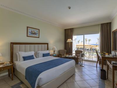 Camera d'hotel luminosa con letto matrimoniale, zona salotto, scrivania e balcone con vista sul mare.