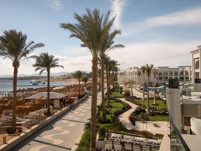 Hotel di lusso con palme e lettini sulla spiaggia sotto un cielo limpido.