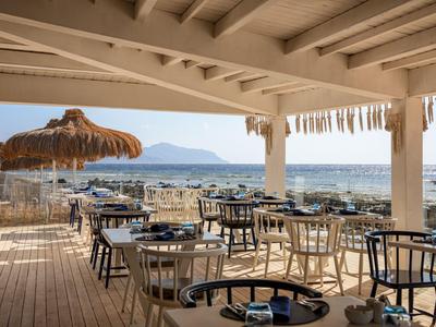 Terrazza coperta di un hotel con tavoli e sedie di legno e vista sul mare e sulle montagne.