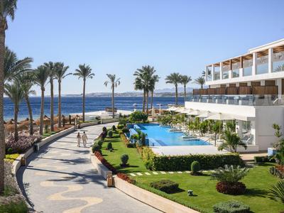 Complexe hôtelier avec piscine, jardin et vue sur la mer par une journée ensoleillée.