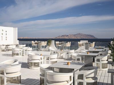 Terrasse blanche moderne avec sièges blancs et vue sur la mer, journée ensoleillée avec île au loin.