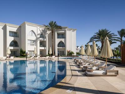 Espace piscine d'hôtel moderne avec transats, parasols et palmiers sous un ciel dégagé.