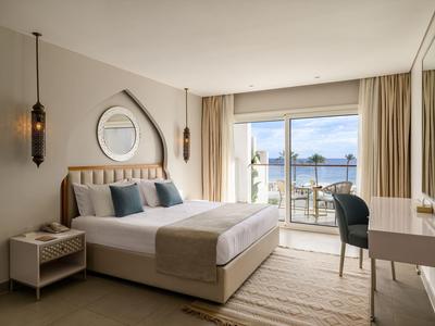 Chambre d'hôtel lumineuse avec lit double, balcon et vue sur la mer en plein jour.