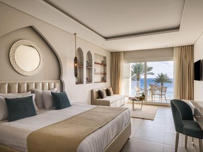 Chambre d'hôtel moderne avec deux lits, coin salon et terrasse donnant sur la mer.