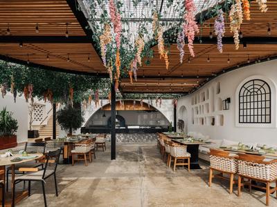 Area pranzo esterna con soffitto in legno, fiori sospesi, sedie imbottite e forno per pizza.