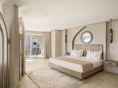 Chambre d'hôtel moderne avec grand lit, tapis et fenêtre ronde donnant sur la terrasse.