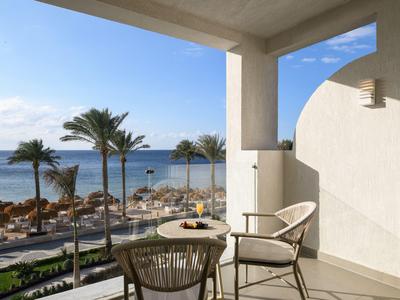 Balcon d'hôtel avec deux chaises et une table donnant sur des palmiers et la mer.