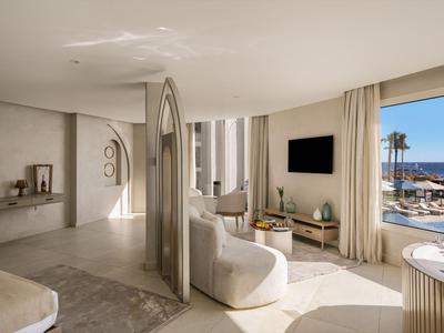 Chambre d'hôtel lumineuse avec canapé incurvé et vue sur la piscine et la mer.